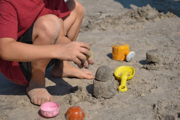 Chłopiec bawi się na plaży w piasku. Dziecko buduje figury piaskowe. Zabawki na plaży. Wesołych świąt nad morzem. — Zdjęcie stockowe