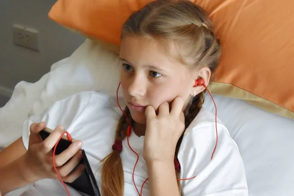 ヘッドフォンで音楽を聞いている女の子。10代は携帯電話でビデオを見ています。電話を持つ子供の女の子 — ストック写真
