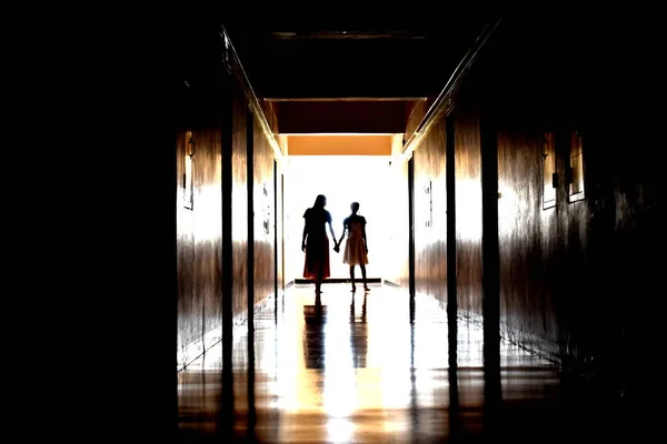Emberek sziluettjei egy hosszú sötét folyosón. Egy nő és egy gyerek szellemei. Sötét hátborzongató folyosó szellemekkel. — Stock Fotó