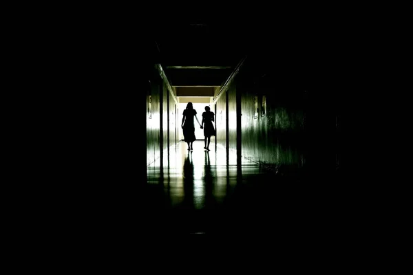 Sylwetki ludzi w długim ciemnym korytarzu. - Duchy kobiety i dziecka. Ciemny straszny korytarz z duchami.. — Zdjęcie stockowe