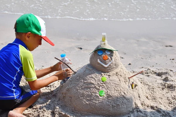 Junge bastelt Sandmännchen am Strand. Das Kind baut einen Schneemann am Strand. Neues Jahr auf dem tropischen Ozean. — Stockfoto