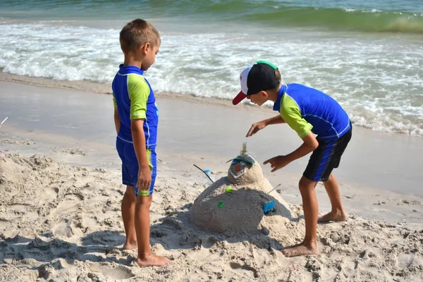 A gyerekfiúk homokembert csinálnak a parton. A gyerek hóembert épít a parton. Új év a trópusi óceánon. — Stock Fotó