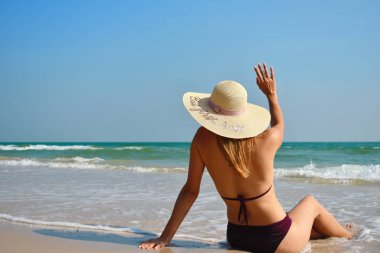 Kumsaldaki şapkalı kız elini kaldırdı. Sahilde arkadaşını bekleyen bir kadın. Denizde mayo giymiş bir kadın.