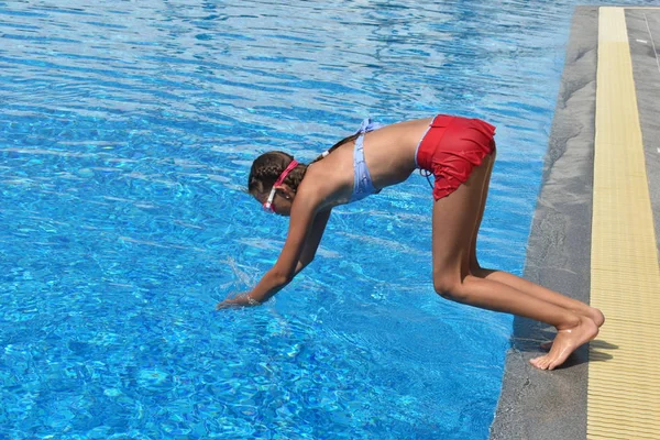 Niña se zambulle en la piscina. Chica aprendiendo a nadar al aire libre. Piscina en el hotel. Niños nadan en la piscina al aire libre . — Foto de Stock