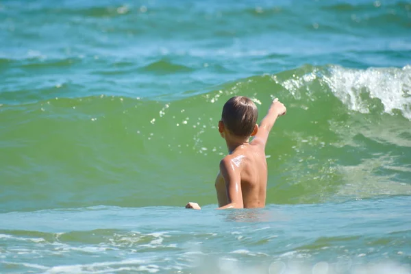 Fiú gyermek játszik a tengerben. Gyerek fröcsköl a vízre. A tengeren töltött nyaralásod. Játékok az óceánban. — Stock Fotó