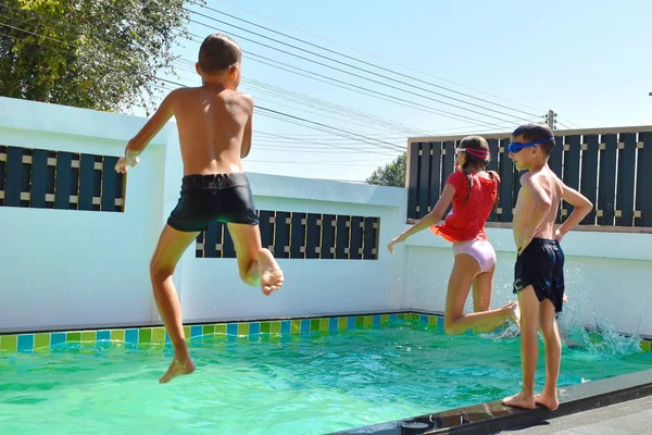 一群孩子跳进游泳池里。快乐的孩子们跳进了房子的私人游泳池里.度假胜地的暑假. — 图库照片