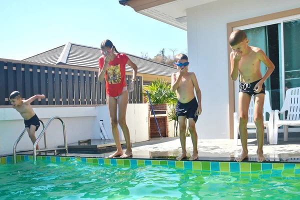 Kindergruppe springt ins Becken. Glückliche Kinder tauchen in den privaten Pool des Hauses. Sommerurlaub im Resort. — Stockfoto