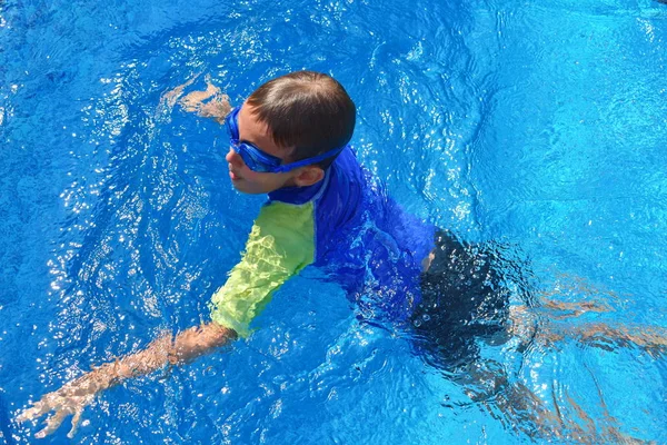 Niño en una piscina azul en el hotel. Niño nada en gafas de sol — Foto de Stock