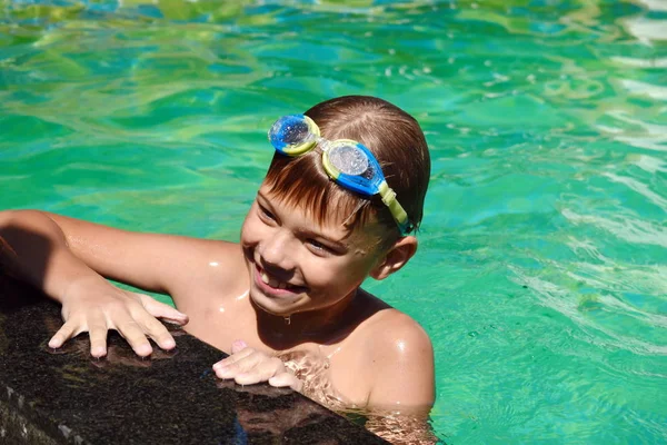 Menino numa piscina azul no hotel. Criança nada em óculos — Fotografia de Stock