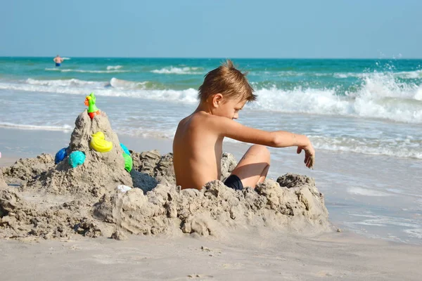 En liten pojke bygger ett sandslott. Leker med sand och leksaker för havet. Semester med barnen på resorten. — Stockfoto