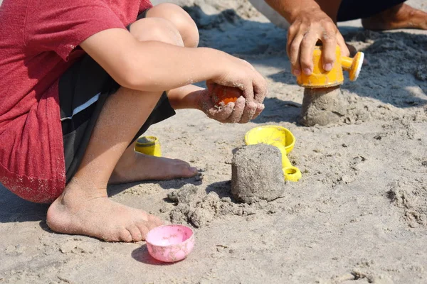 Seorang anak kecil membangun istana pasir. Bermain dengan pasir dan mainan untuk laut. Sebuah liburan dengan anak-anak di resor . — Stok Foto