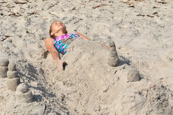 Kleines Mädchen auf dem Sand liegend. Kinder mögen Mumien am Strand. — Stockfoto