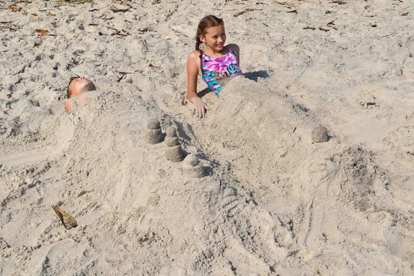 모래 위에 누워 있는 어린 소녀. 해변에서 미이라를 좋아하는 아이들. — 스톡 사진