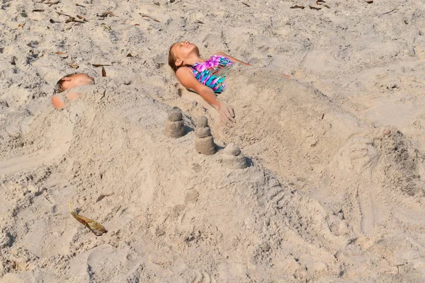 Egy kislány fekszik a homokban. A gyerekek szeretik a múmiákat a parton.. — Stock Fotó