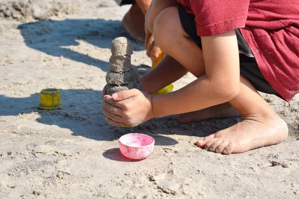 Seorang anak kecil membangun istana pasir. Bermain dengan pasir dan mainan untuk laut. Sebuah liburan dengan anak-anak di resor . — Stok Foto