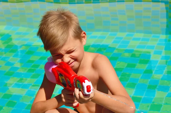 Menino com uma arma de água. Crianças brincam na piscina. — Fotografia de Stock