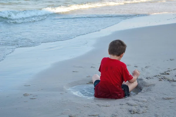 En liten pojke som leker i sanden. Ligger i en sandpöl. lek i leran. — Stockfoto