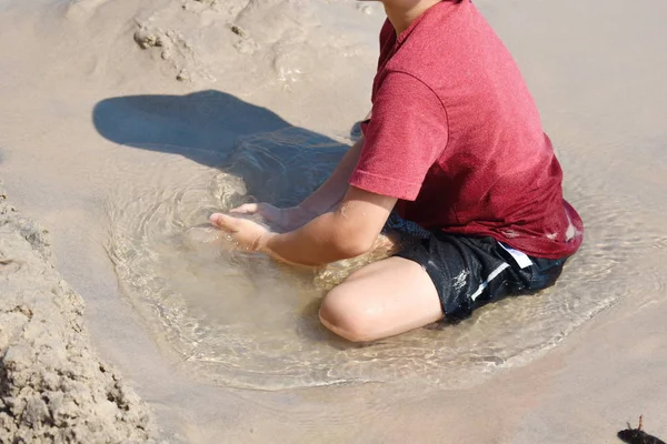 Een jongetje dat in het zand speelt. Liggend in een zandplas. spelen in de modder. — Stockfoto