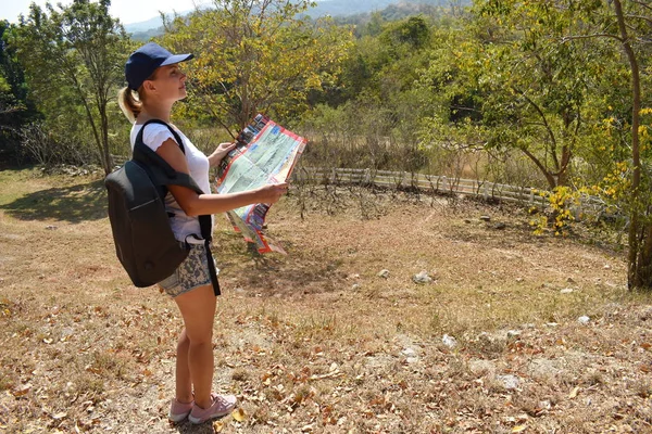 Egy fiatal lány egy útitervvel az erdőben. Egy utazó a hegyekben keresi az utat. Útmutató az útitervhez. — Stock Fotó