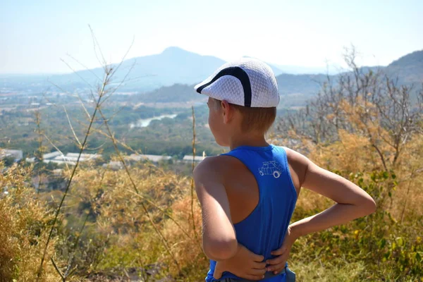 The boy child looks at the mountains. The kid in the cap camper on the mountain. — ストック写真