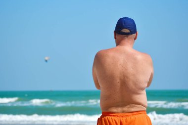 Yetişkin bir adam orada durmuş denize bakıyor..