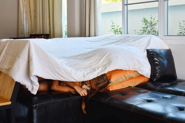 Meisje in het huis uit dekens. Het meisje onder de deken op het bed. — Stockfoto