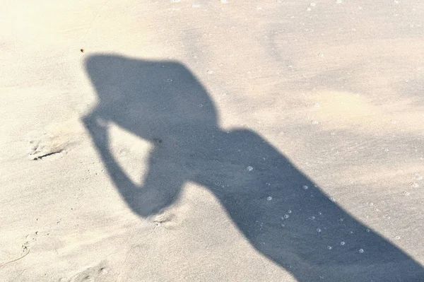 Sombra de chica con sombrero en el suelo. Una mujer se refleja en la arena mojada — Foto de Stock
