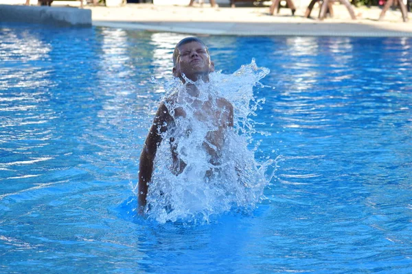 Un chico se zambulle en la piscina del hotel. Diversión con los niños en el resort. El niño salta del agua . — Foto de Stock