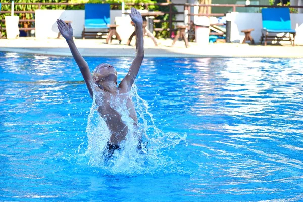 Um rapaz mergulha na piscina do hotel. Diversão com as crianças no resort. A criança salta da água . — Fotografia de Stock