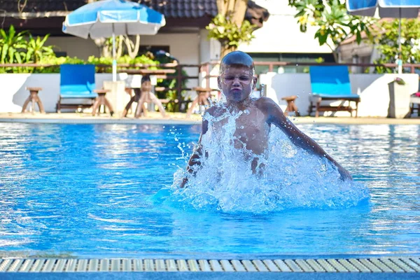 Chlapec se vrhne do bazénu v hotelu. Zábava s dětmi v letovisku. Dítě vyskočí z vody.. — Stock fotografie