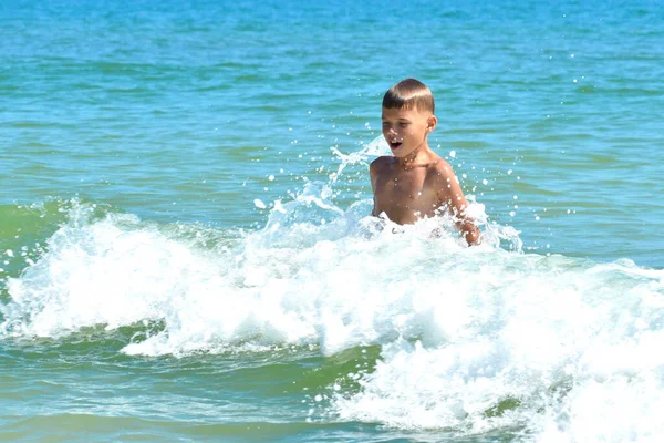 Un ragazzino che gioca nell'acqua di mare. Un bambino salta dal mare. Una vacanza tropicale con bambini . — Foto Stock