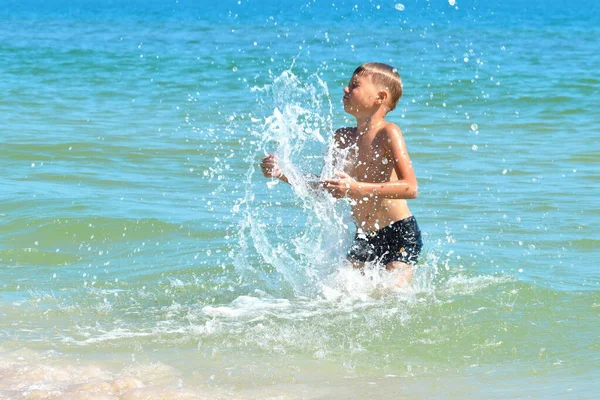 Маленький мальчик играет в морской воде. Ребенок прыгает с моря. Тропический отдых с детьми . — стоковое фото
