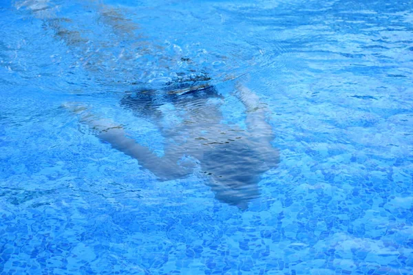 男孩在酒店开放的蓝色游泳池中漂浮在水下。 在水下搜寻. — 图库照片
