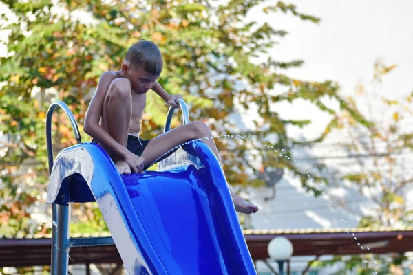 Seorang anak laki-laki duduk di atas air slide di kolam renang . — Stok Foto