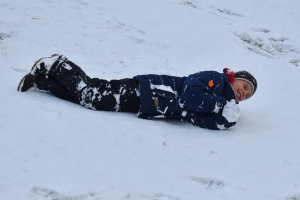 Ein lustiger Winter. Kind rollt im Schnee. Junge liegt im Winter im Schnee. — Stockfoto