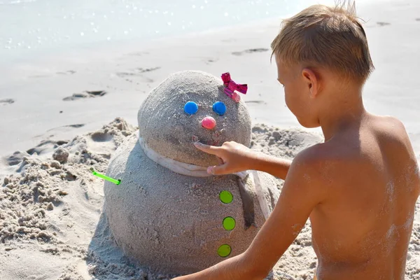 Дитина і сніговик на пляжі. Новий рік у приморському курорті . — стокове фото