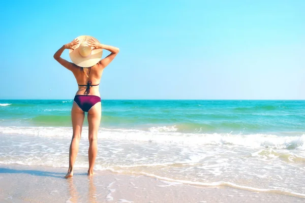 Γυναίκα με καπέλο στην παραλία. Κορίτσι με μαγιό στον ωκεανό. Τροπικές καλοκαιρινές διακοπές — Φωτογραφία Αρχείου