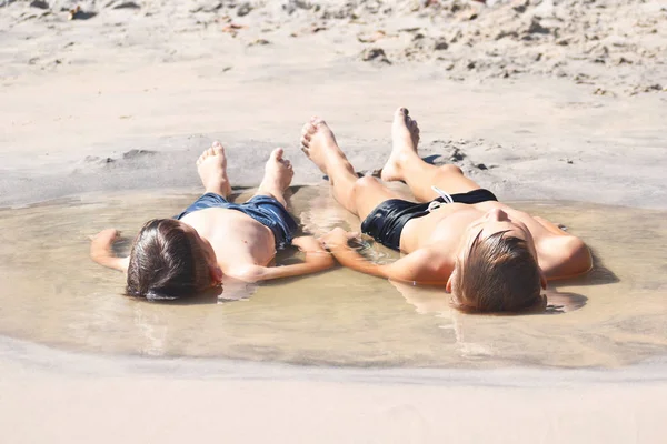 Дети лежат на песке. Мальчики загорают в воде. Детство в луже. Прямой ребенок — стоковое фото