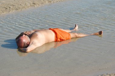 Sahildeki su birikintisindeki adam. Deniz kenarında dinleniyorum. Eğlenceli plaj fotoğrafı. Denizdeki şişman adam.