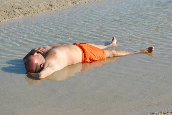 Der Mann in der Pfütze am Strand. erholsame Ferien am Meer. Spaßiges Strandfoto. der dicke Mann im Meer — Stockfoto