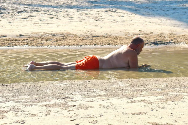 The man in the puddle on the beach. Relaxing holiday by the sea. Fun beach photo. The fat man in the sea — 스톡 사진