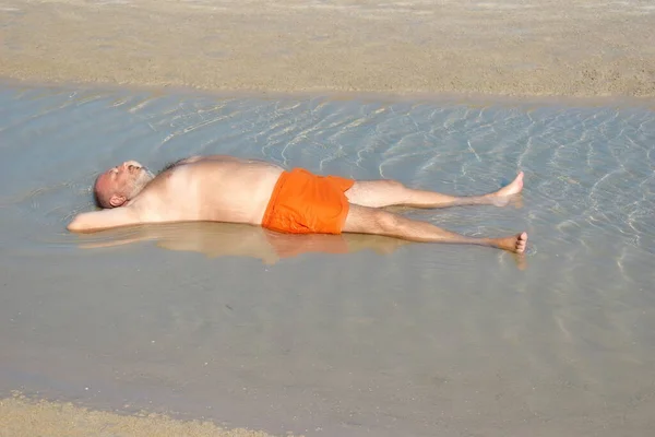 Der Mann in der Pfütze am Strand. erholsame Ferien am Meer. Spaßiges Strandfoto. der dicke Mann im Meer — Stockfoto