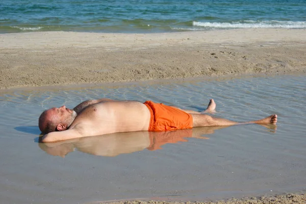 El hombre en el charco en la playa. Vacaciones relajantes junto al mar. Foto de playa divertida. El gordo en el mar —  Fotos de Stock