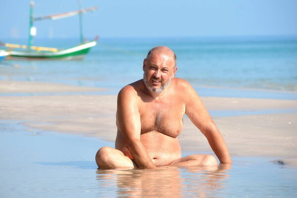 The man in the puddle on the beach. Relaxing holiday by the sea. Fun beach photo. The fat man in the sea