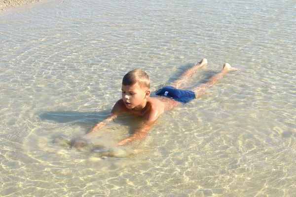 Çocuk bir su birikintisinde yatıyor. Aletsiz mutlu bir çocukluk. Çamurda neşeli bir çocuk. — Stok fotoğraf