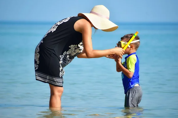 Modern till pojken i badorten. Mor och barn vid havet. Mor sätter vattenglasögon. — Stockfoto