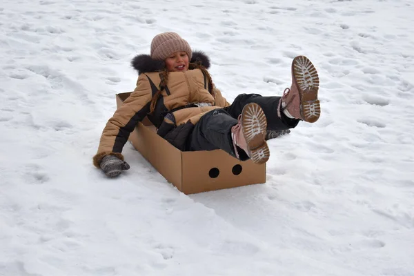 Mädchen in einem Karton auf einem Hügel im Winter. Kind, um im Winter Spaß zu haben. Winter ist lustiges Spiel. Sportliche Feiertage zu Weihnachten. — Stockfoto