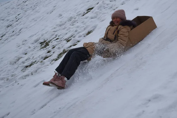 Chica en una caja de cartón en la colina en invierno. Niño para divertirse en invierno. El invierno es divertido juego. Vacaciones deportivas en Navidad . —  Fotos de Stock