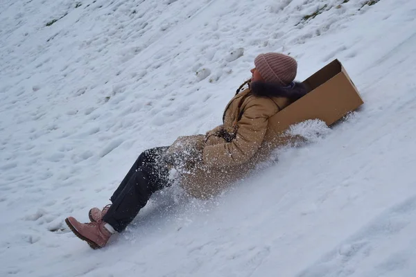Mädchen in einem Karton auf einem Hügel im Winter. Kind, um im Winter Spaß zu haben. Winter ist lustiges Spiel. Sportliche Feiertage zu Weihnachten. — Stockfoto