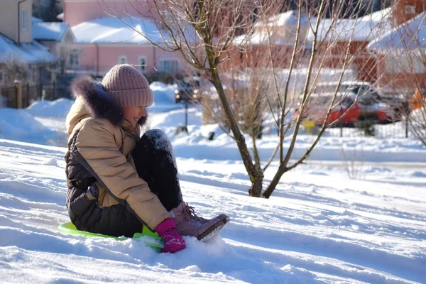 Mädchen auf einem Schlitten im Schnee. frohe Winterferien. Lustige Babyrutsche im Winter — Stockfoto